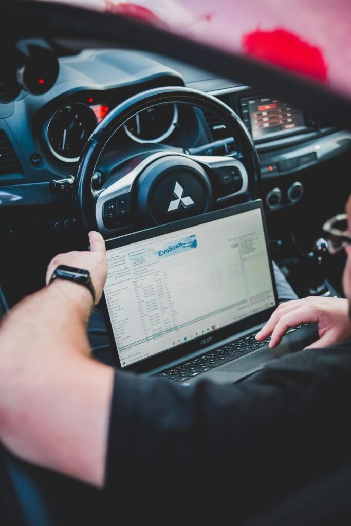 A person using a laptop inside a car for vehicle diagnostics, showcasing technology integration in automotive settings.